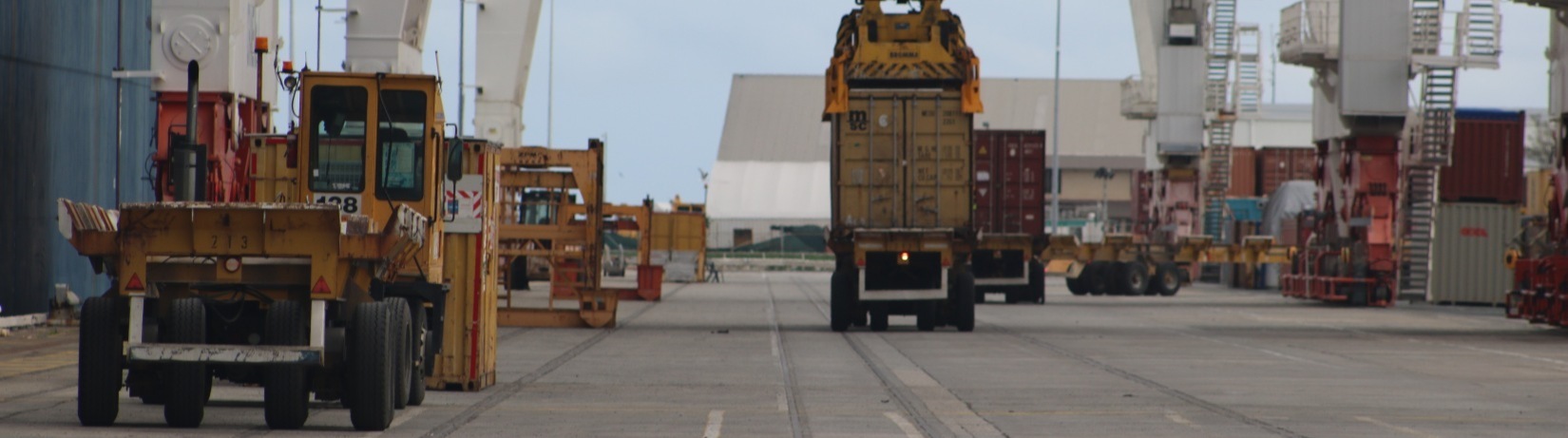 Trucks being loaded with containers by ship-to-shore cranes at a port.
