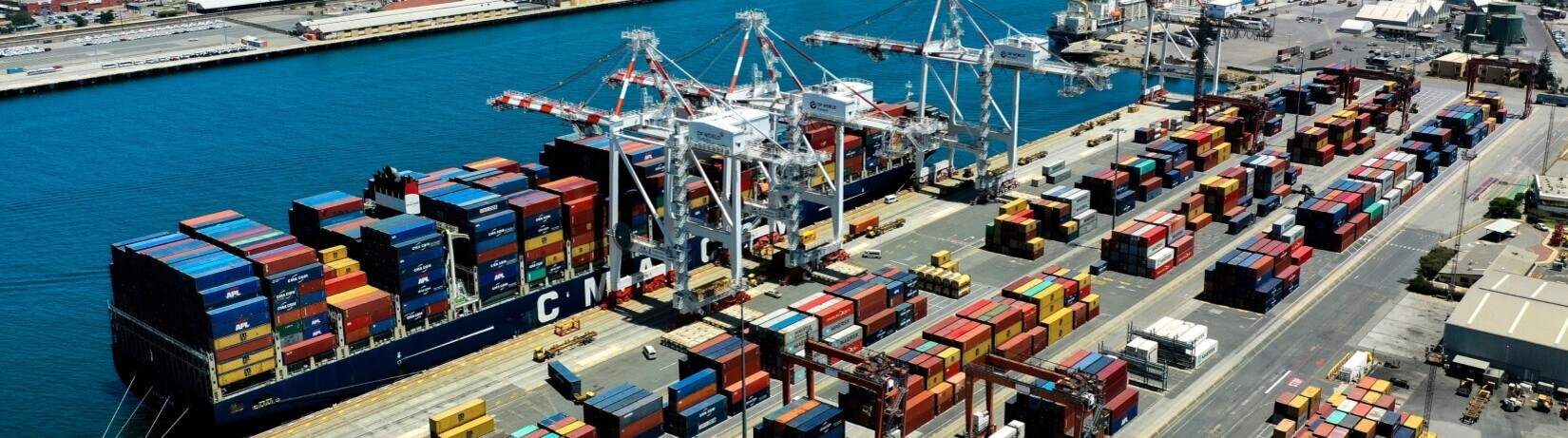 Aerial photo of a container vessel being unloaded by ship-to-shore cranes, additional stacks of container are in view landside.