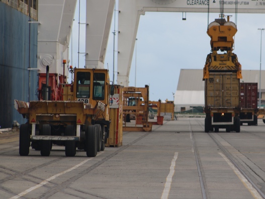 Photo of container trucks being loaded by a ship-to-shore crane.