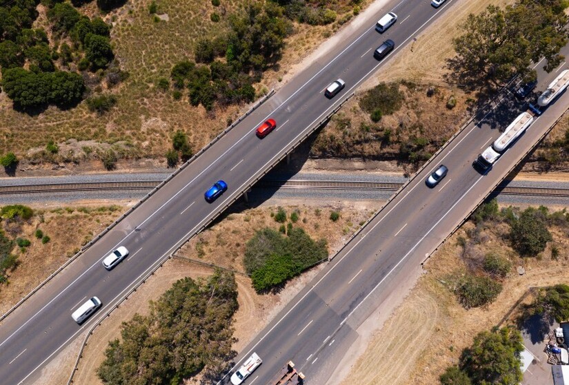 Bird's eye view of dual road overpasses over a rail line.