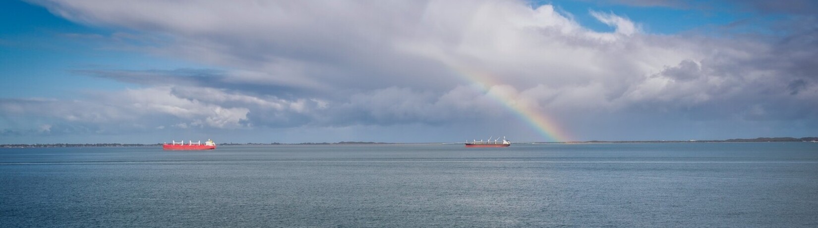 Photos of vessels in the Cockburn Sound, a rainbow is in the background breaking through the clouds. 