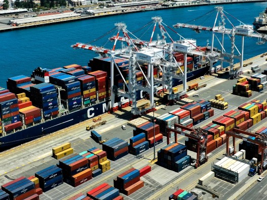Aerial photo of containers being unloaded off a container vessel by ship-to-shore cranes.